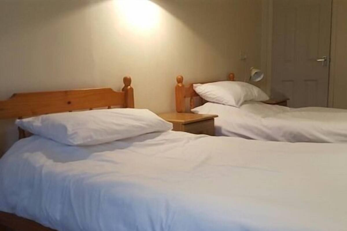 A room with two single beds, each with wooden headboards and white bedding. There is a nightstand with a lamp on one side.