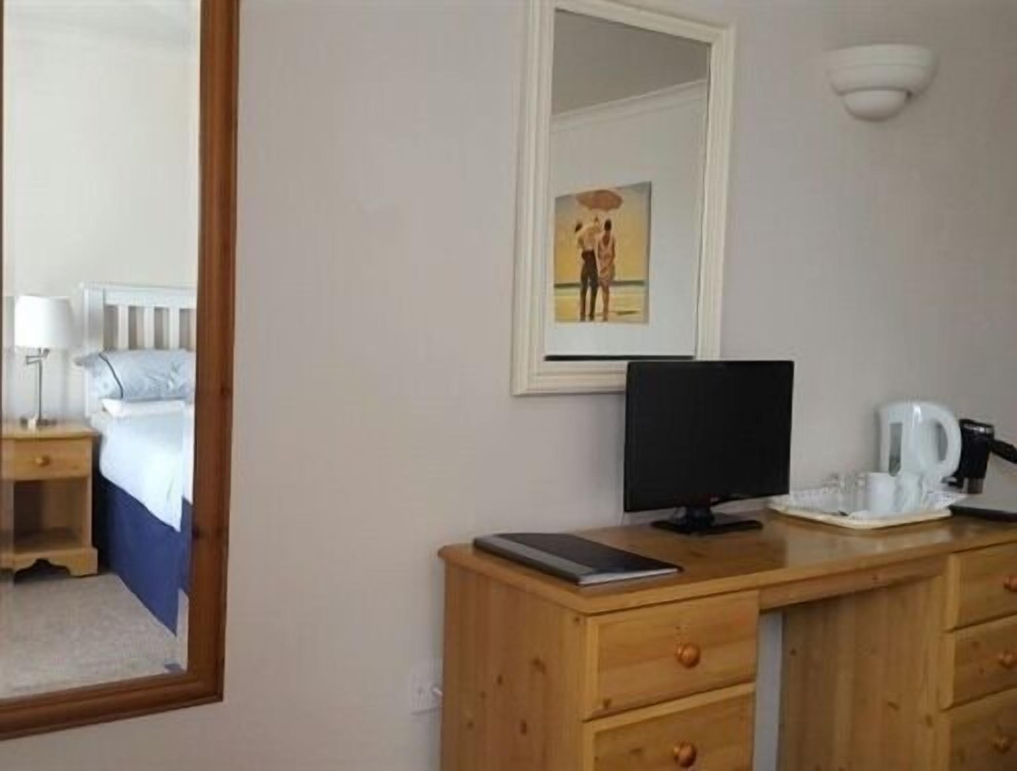 A hotel room with a bed, a desk with a computer, a coffee maker, and a framed picture on the wall.