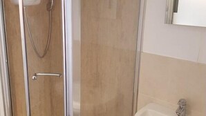 A glass-enclosed shower stall with a handheld showerhead, a door with a silver handle, and a white sink with a faucet. - A35 PitStop (Axminster)