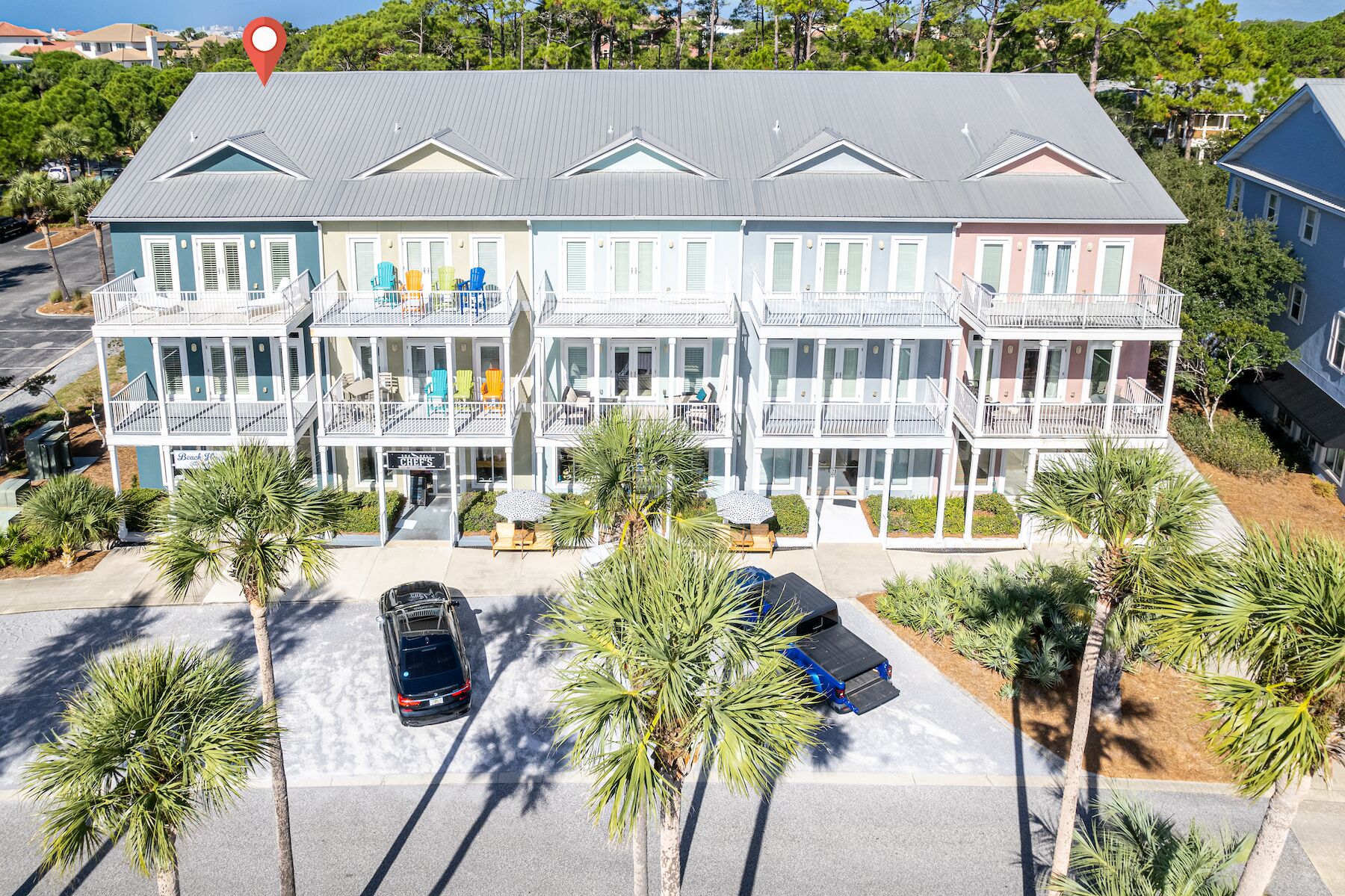 A multi-story hotel with balconies, a beach sign, and parked cars.