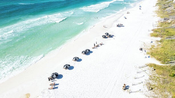 Una playa con arena blanca, agua turquesa cristalina y sombrillas.