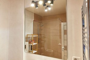 A modern bathroom with a glass-enclosed shower, a white bathtub, and a wooden shelf with toiletries. - Alma Zev Apartment (Navodari)