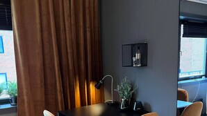 Habitació moderna amb una paret gris fosca, escriptori negre, dues cadires beix i una làmpada negra, amb una finestra i cortines marrons.