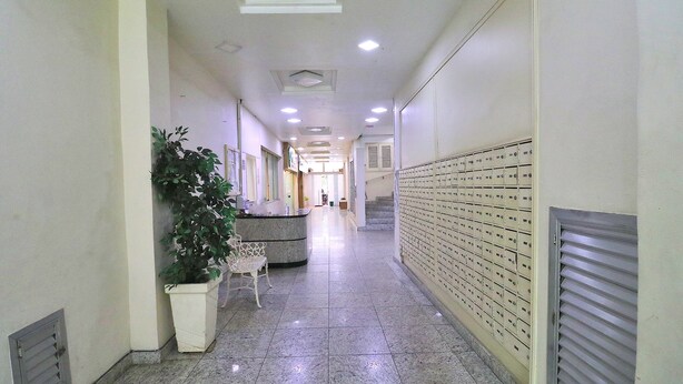 A hallway with a reception desk, a potted plant, a chair, and a row of mailboxes. - Santa Clara Studio (Rio de Janeiro)