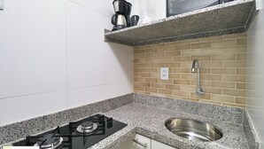 A kitchen with a gas stove, a stainless steel sink, and a countertop with a coffee maker and blender. - Santa Clara Studio (Rio de Janeiro)
