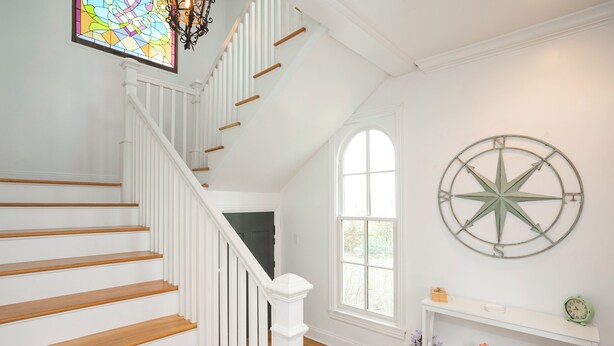 A staircase with white railings and wooden steps, a large arched window, and a wall-mounted compass. - Private, 2 Bedroom Suite with Balcony at Farmhouse Retreat, Central Location (Nashville)