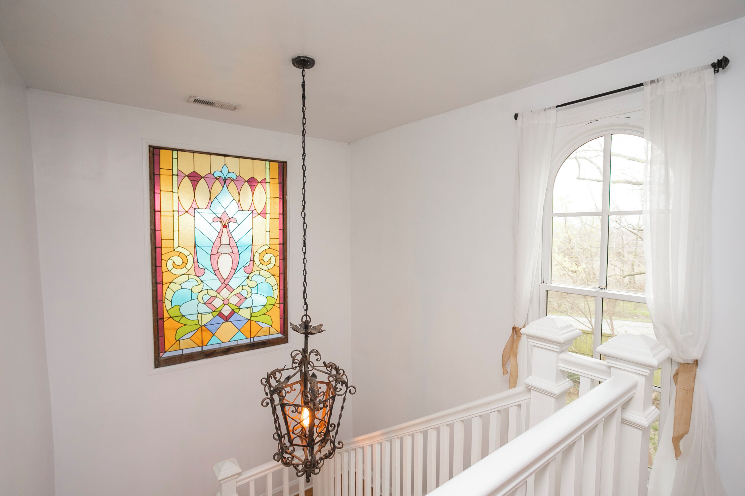 Una escalera con barandillas blancas, una ventana de vitral y un colgador de luces.