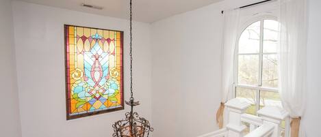 Una escalera con barandillas blancas, una ventana de vitral y un colgador de luces.