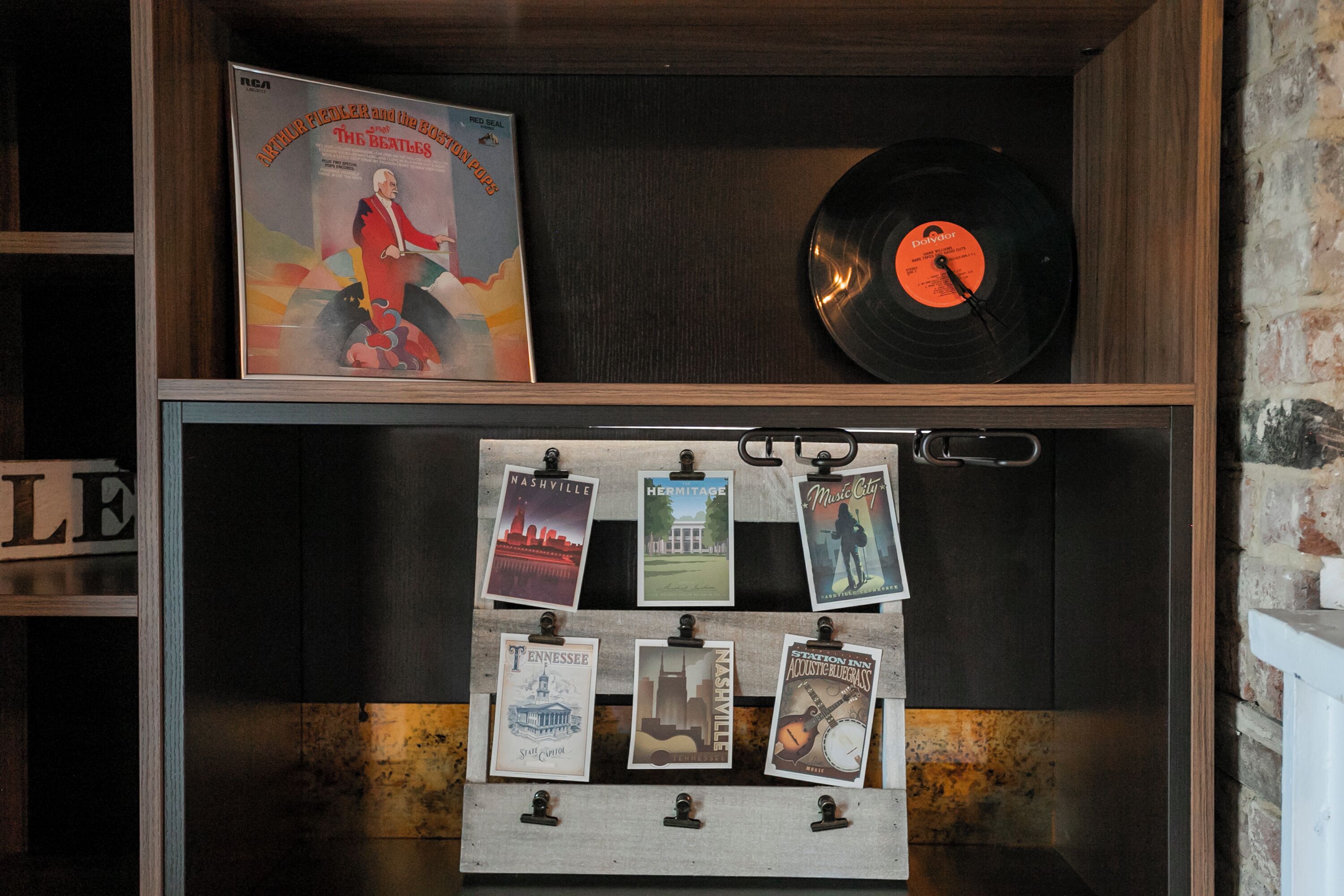Een houten plank met een vinylplaat en een ingelijste poster. Daaronder, zes ansichtkaarten vastgemaakt aan een prikbord.