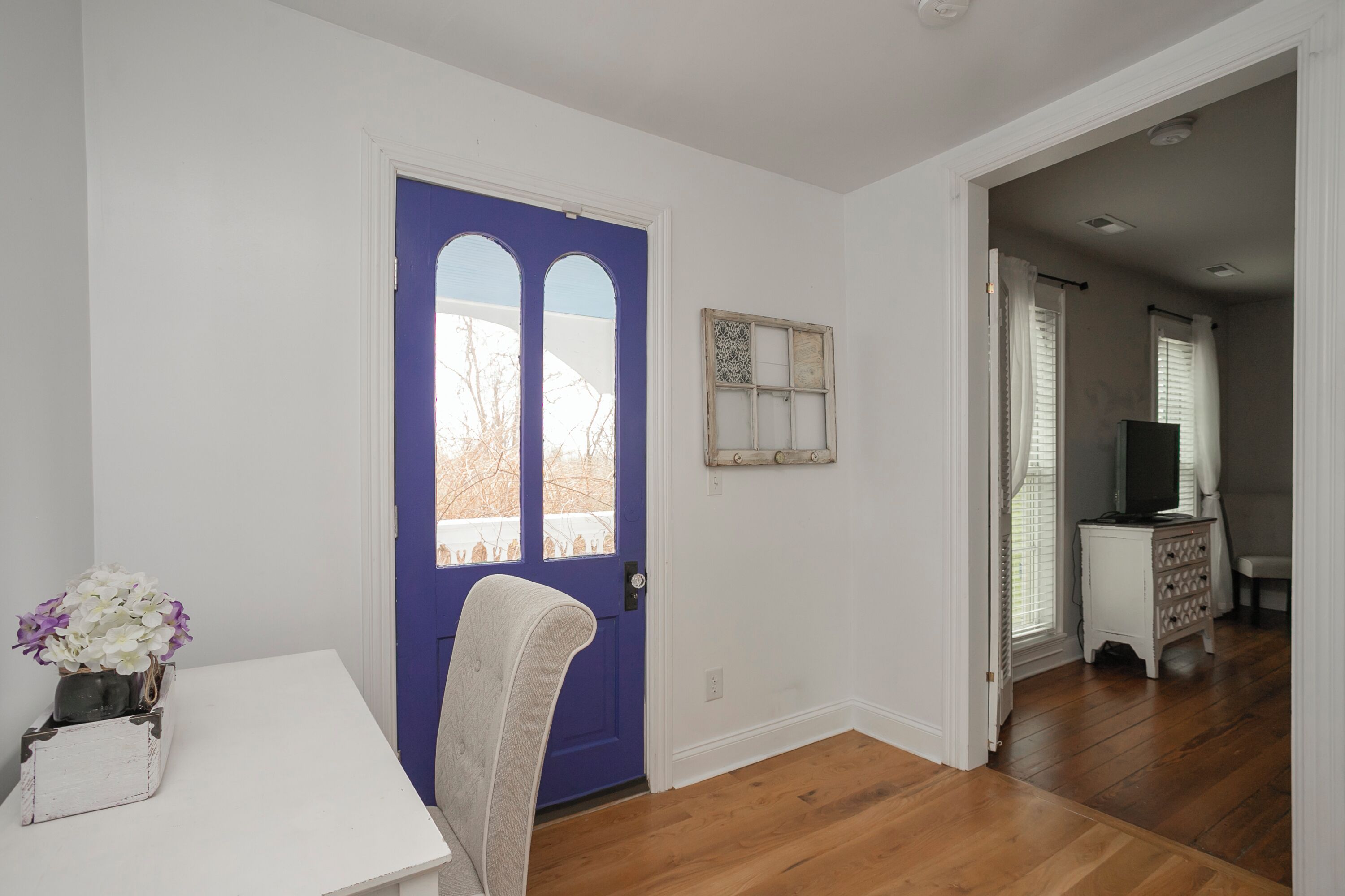 A room with a blue door, a white table with a vase of flowers, and a wooden floor.