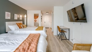 A hotel room with two beds, a desk, a chair, a television, and artwork on the walls. - Room 204 - Two Queens - Kitchenette - NonSmoking (Lincoln)