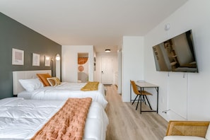 Une chambre d’hôtel avec deux lits, un bureau, une chaise, une télévision et des œuvres d’art accrochées aux murs.
