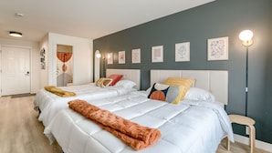 Une chambre avec deux lits, une tête de lit blanche et un mur d’accent de couleur grise.