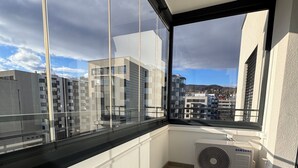 Een balkon met een Samsung air conditioner, uitzicht op gebouwen en een betegelde vloer.