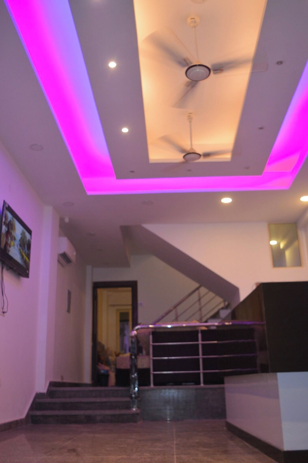 Een modern interieur met een plafondventilator, roze verlichting en een trap.