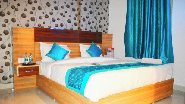 Een net opgemaakt bed met een houten hoofdbord, twee kussens en een blauw sierkussen. Er staat een nachtkastje met een fles en een klein doosje naast het bed.
