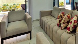 A living room with a sofa, a chair, and a dining table with chairs. - Casa 11 Villa Giardino-SH033 (Tamandaré)