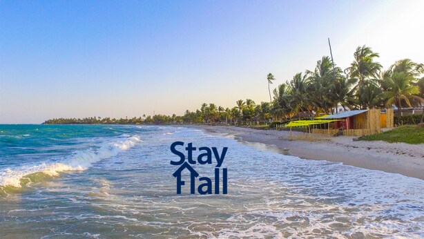 A beach with clear waters, a sandy shore, and a row of palm trees. The text "Stay Hall" is visible on the beach. - Casa 11 Villa Giardino-SH033 (Tamandaré)