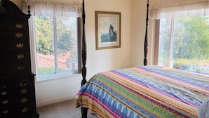 A bedroom with a large bed, a dark wooden dresser, and a window with a view of trees.