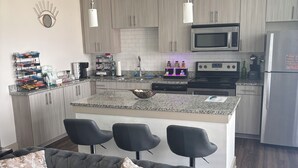 Eine moderne Küche mit einer zentralen Kochinsel, schwarzen Barhocker und einem grauen Sofa mit gemusterten Kissen.