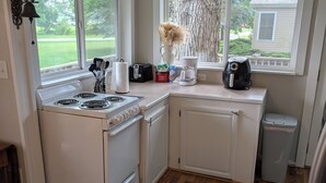 Una cocina con armarios blancos, estufa, cafetera y cubo de basura.