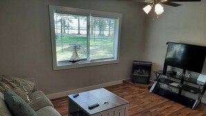 Una sala de estar con sofá, una mesa de centro, un mueble para televisión y una ventana con persianas.