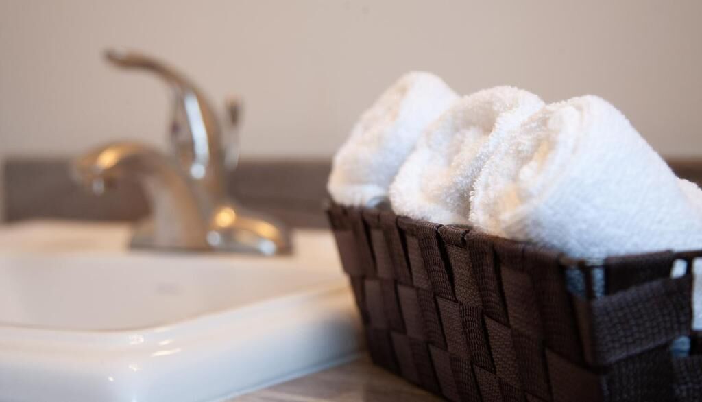 A bathroom sink with a dark woven basket containing white towels.