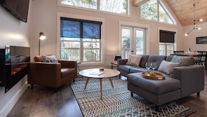 A spacious living room with a fireplace, large windows, and a high ceiling. - Indian Falls Chalets  (Springdale)