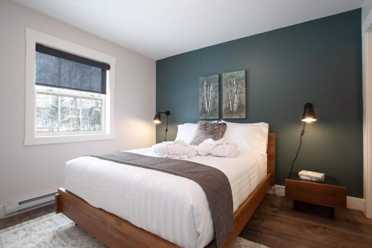 A bedroom with a large bed, two bedside lamps, a window with a view, and two wall-mounted artworks.