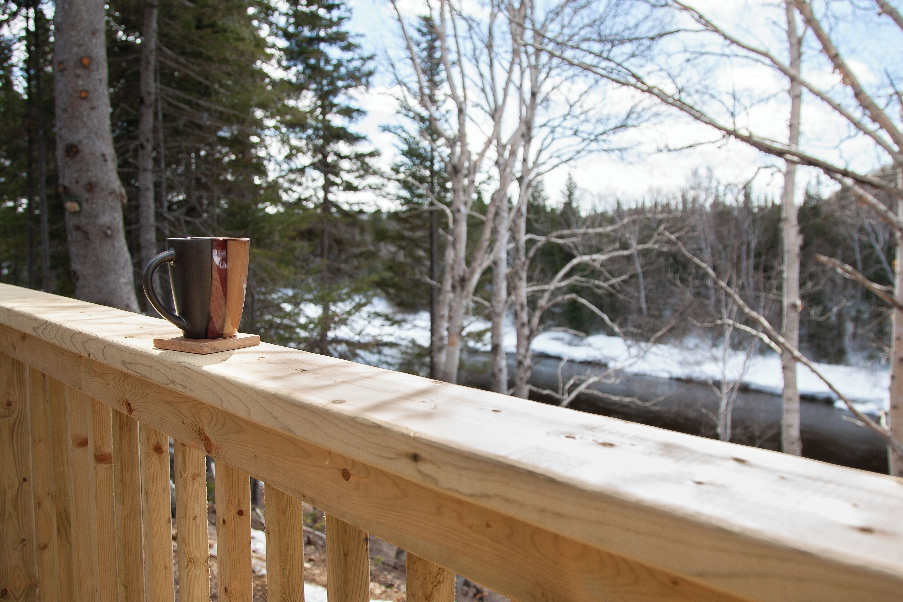 A wooden deck with a metal cup on a coaster.