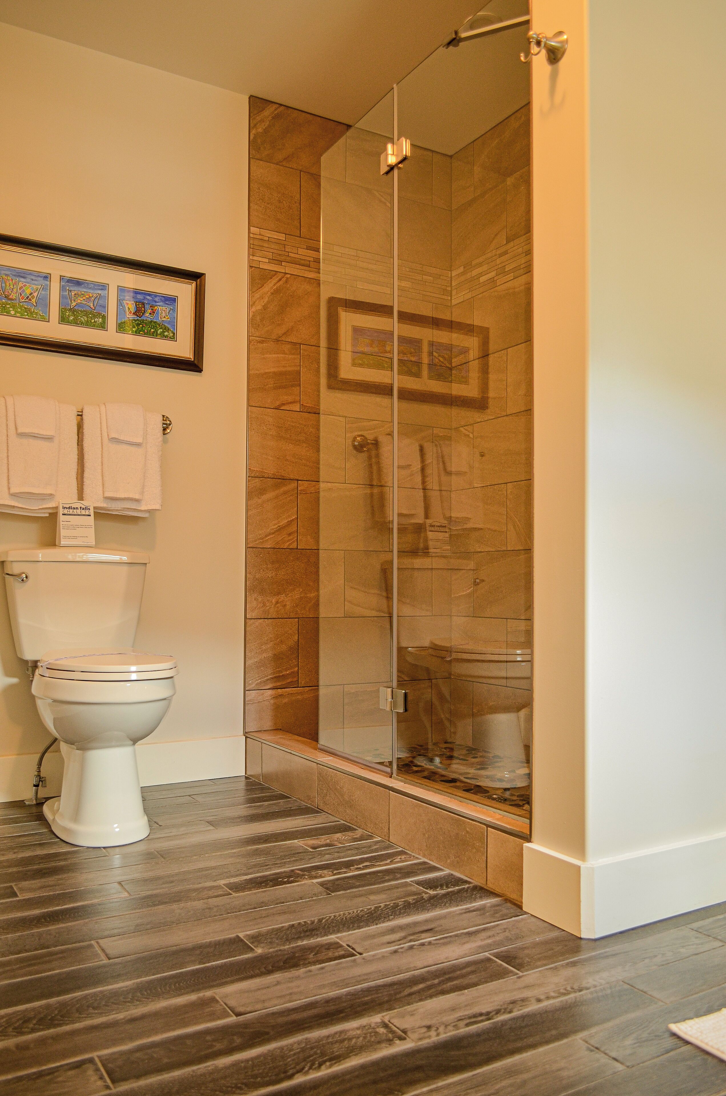 Un baño con ducha de vidrio, inodoro y piso de madera.