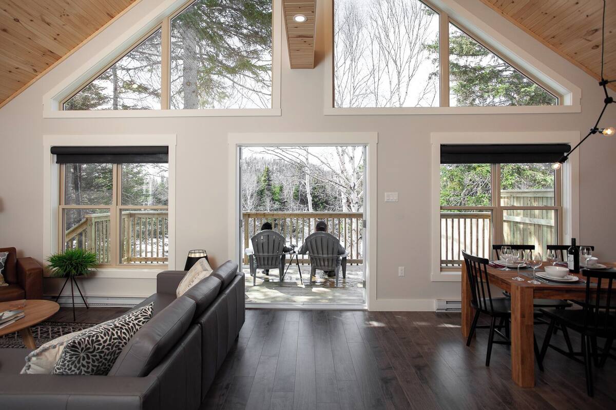 A spacious living room with a high ceiling, large windows, and a view of a deck area.