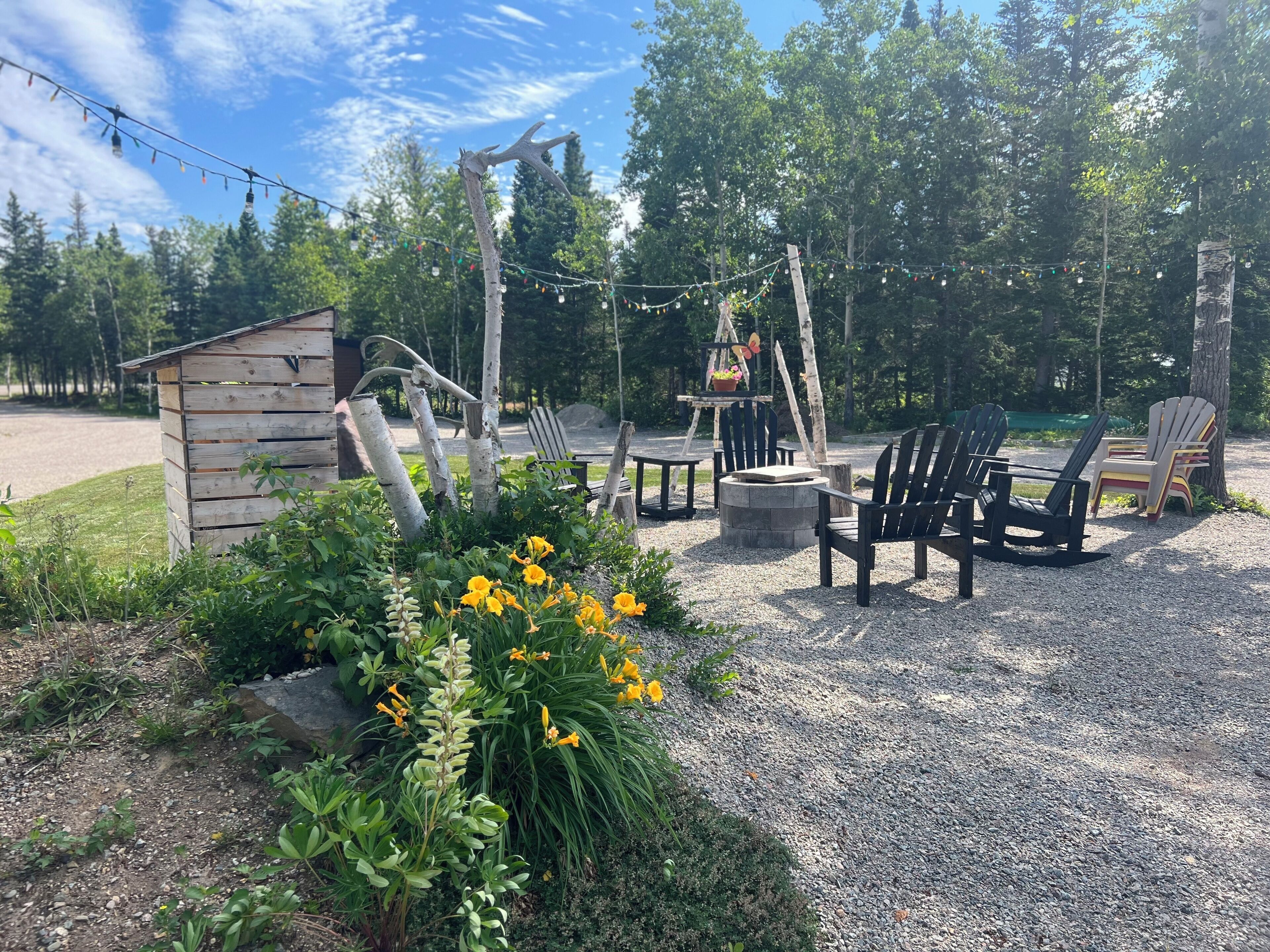 A rustic outdoor seating area with Adirondack chairs, a small wooden structure, and a fire pit.