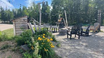 A rustic outdoor seating area with Adirondack chairs, a small wooden structure, and a fire pit.