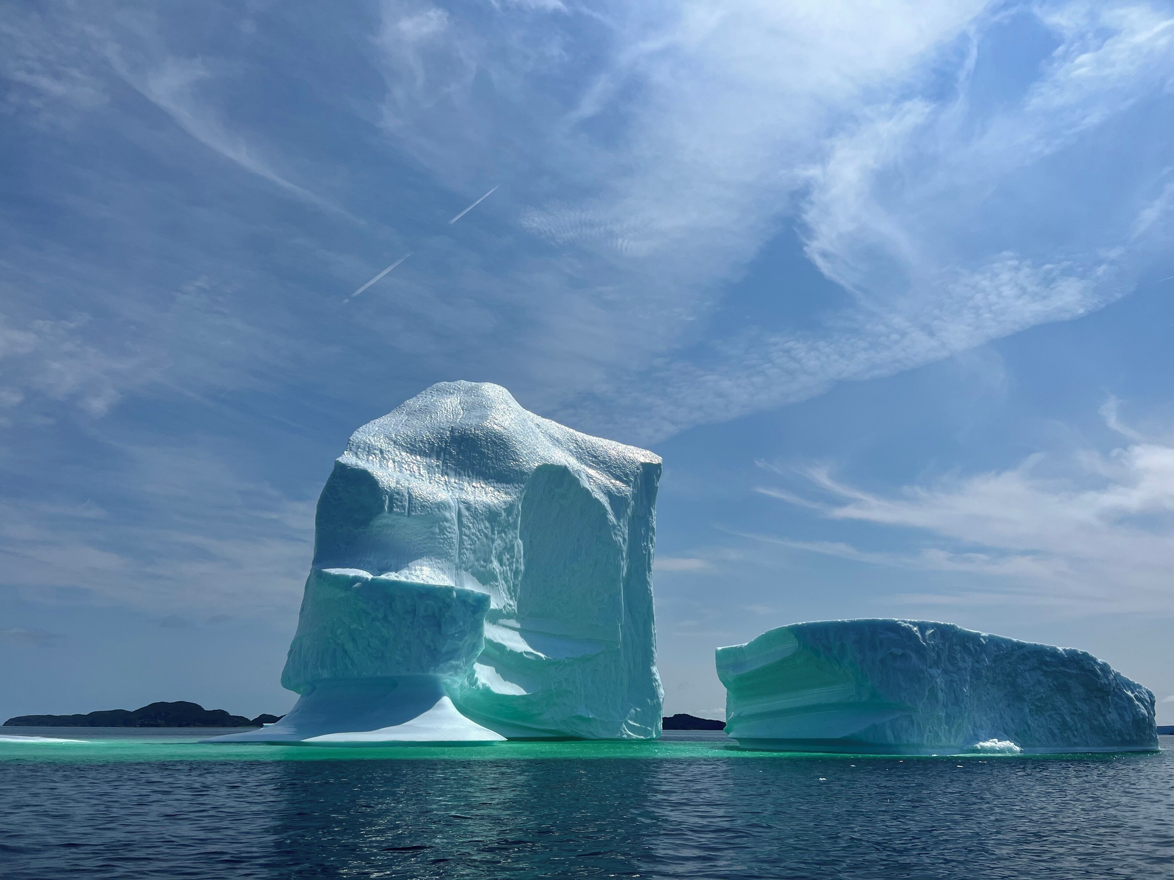 A large iceberg in clear waters with a distant landmass.