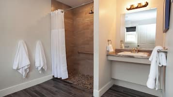 A modern bathroom with a shower, a vanity with a mirror, and towels hanging on the wall.
