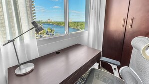 A modern room with a desk, a chair, a lamp, and a view of a river and buildings. - Eternal Sunrise (Fort Lauderdale)