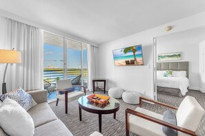 A hotel room with a large window, a sofa, a coffee table, a bed, and a painting of a beach scene. - Eternal Sunrise (Fort Lauderdale)