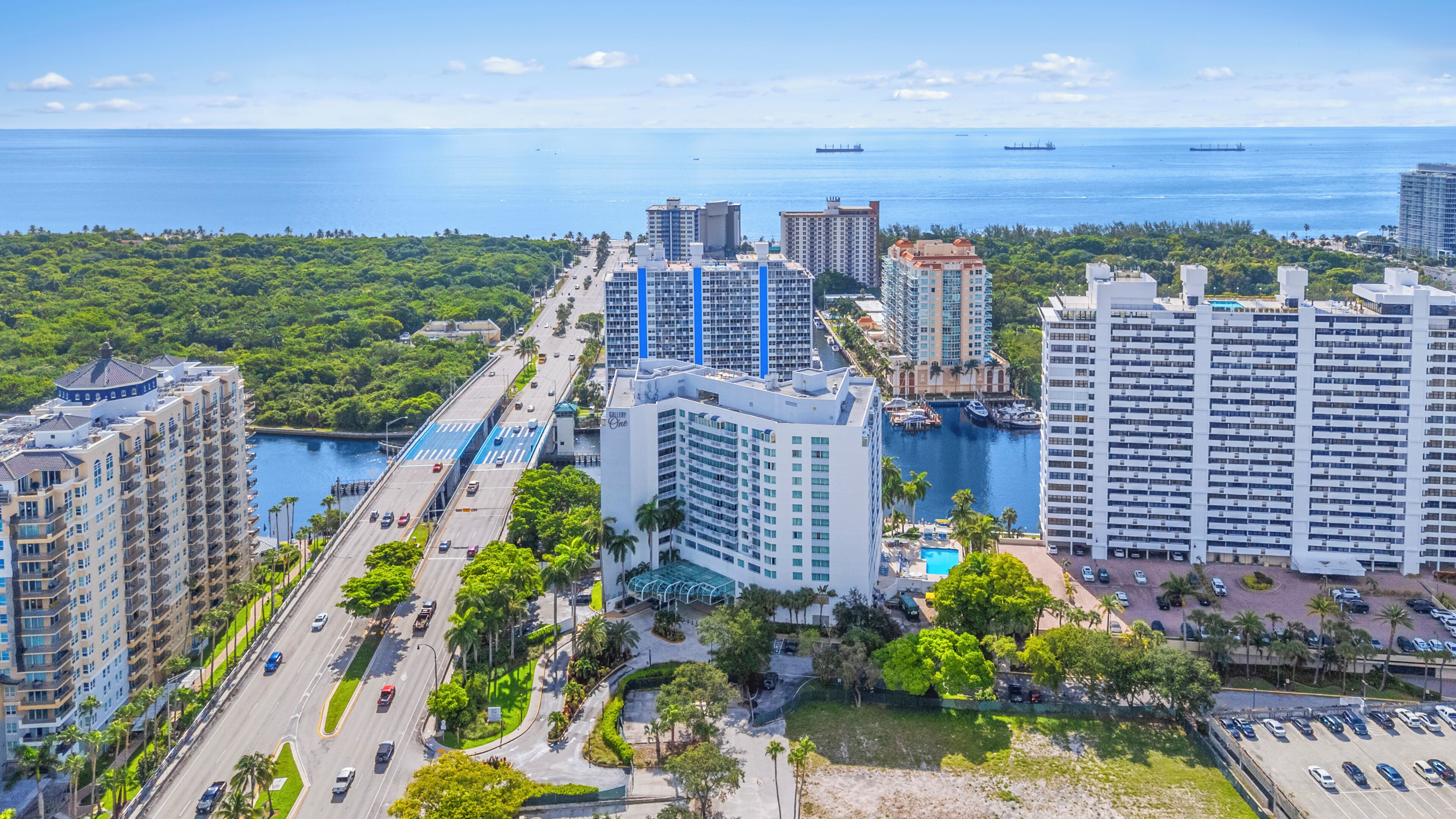 A high-rise hotel with a marina, a road with vehicles, and a view of the ocean.