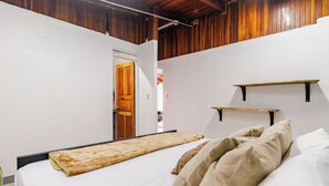 Een slaapkamer met een bed, kussens, een houten deur en een witte muur.