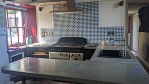 A kitchen with a gas stove, oven, and a sink. There is a window with a view outside, and the walls are decorated with patterned tiles. - Charming cottage on the River Boyne,Fishing ,Kayaking,World Heritage sites (Slane)
