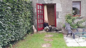 A stone building with a red door, a small porch with two plastic chairs, and a glass table. - Charming cottage on the River Boyne,Fishing ,Kayaking,World Heritage sites (Slane)