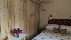 A bedroom with a wooden wall, a bed with a patterned headboard, a bedside table with a basket, and a vase with flowers. - Charming cottage on the River Boyne,Fishing ,Kayaking,World Heritage sites (Slane)