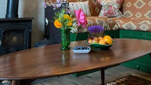 A cozy living room with a wooden ceiling, a sofa with patterned cushions, a table with a vase of flowers, and a bowl of fruit. - Charming cottage on the River Boyne,Fishing ,Kayaking,World Heritage sites (Slane)