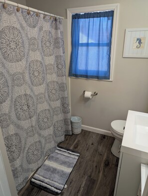 A bathroom with a patterned shower curtain, a blue window, a toilet, and a sink.