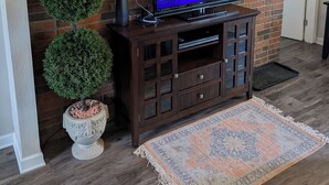 Una sala de estar con pared de ladrillo, un televisor de pantalla plana, un mueble de madera para entretenimiento y objetos decorativos.