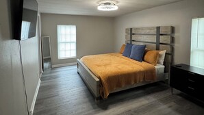 Een slaapkamer met een bed, een aan de muur bevestigde televisie, een dressoir en een plafondlamp.