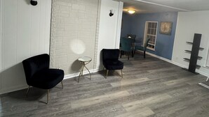 Een ruime kamer met een witte baksteenmuur, een houten vloer en twee zwarte stoelen.