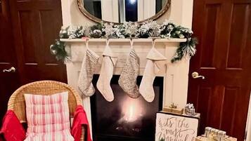 Una sala de estar acogedora con chimenea, un sillón rojo, medias, un coche de juguete y un árbol de Navidad.