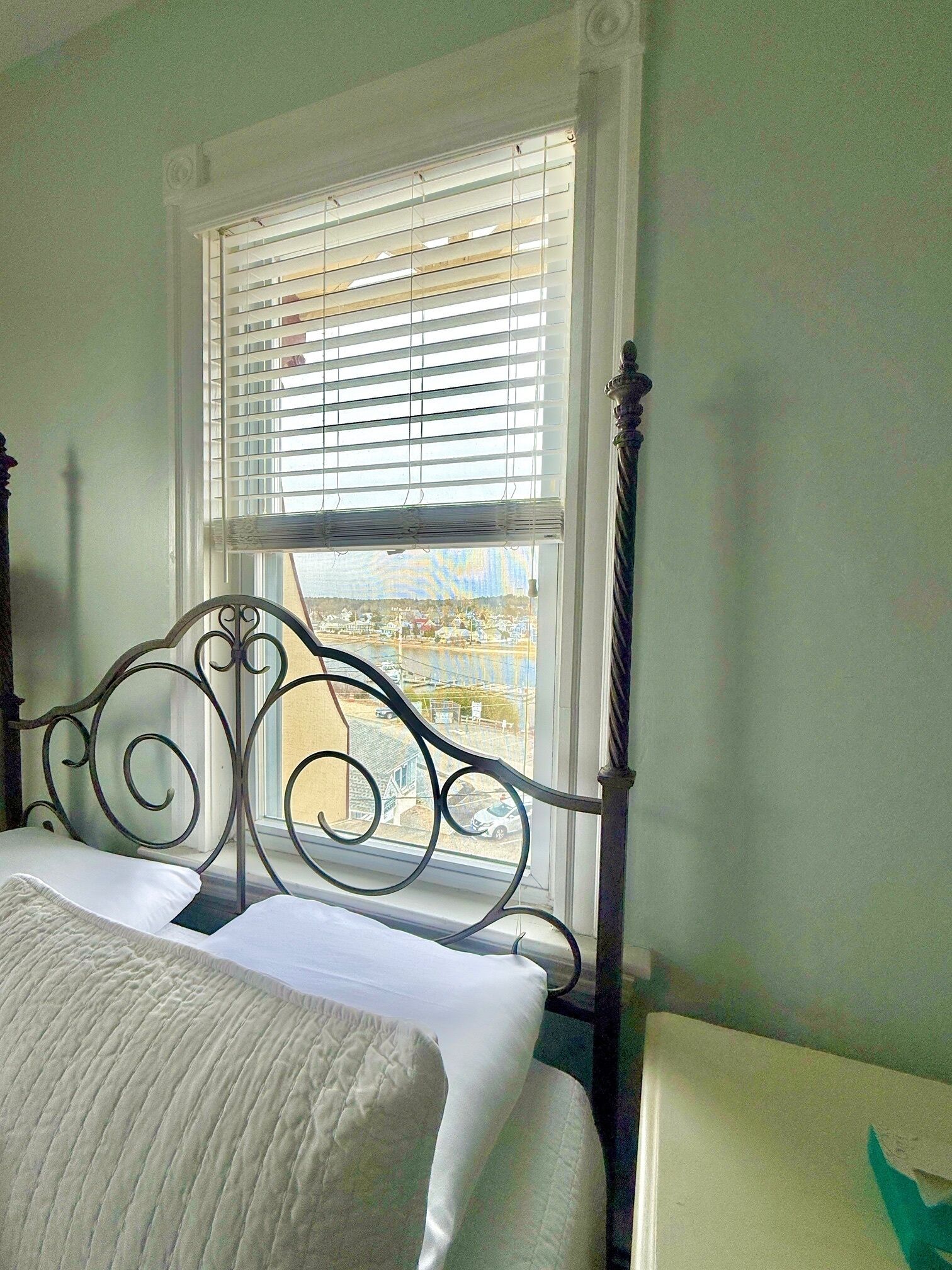 A bedroom with a bed, a window with blinds, and a view of a town.